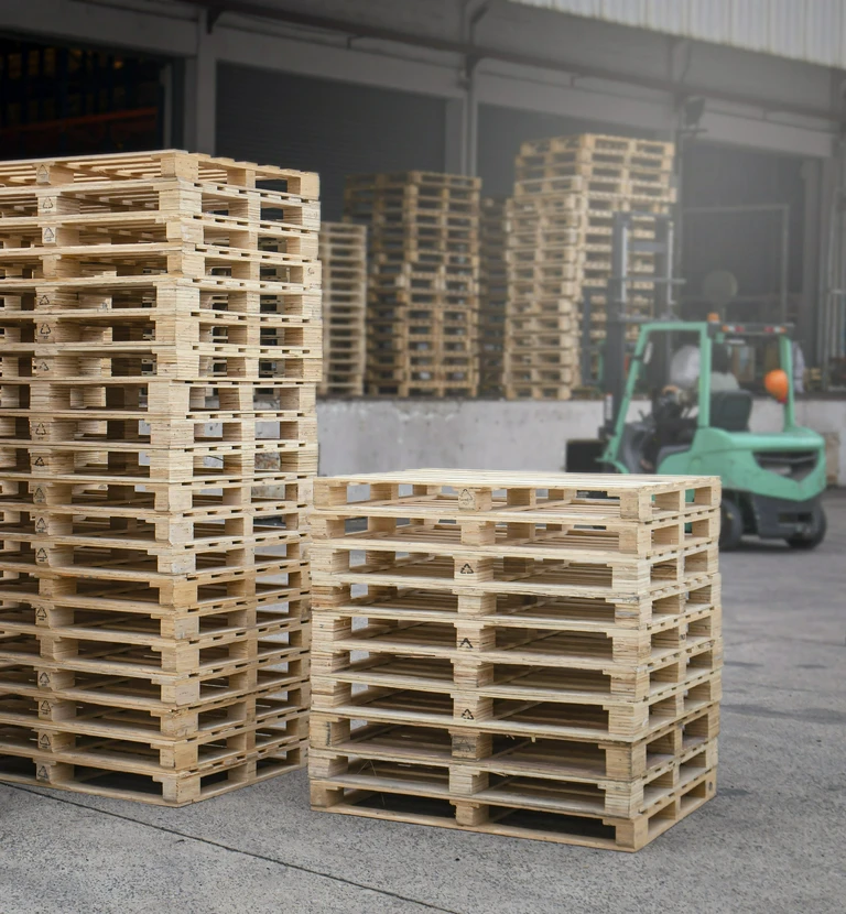Palety drewniane z&nbsp;wózkiem widłowym w&nbsp;tle